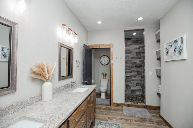 full bathroom featuring toilet, wood finished floors, a sink, tiled shower, and double vanity