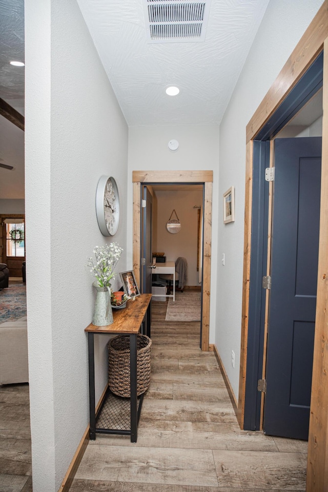 hall with baseboards, visible vents, and wood finished floors