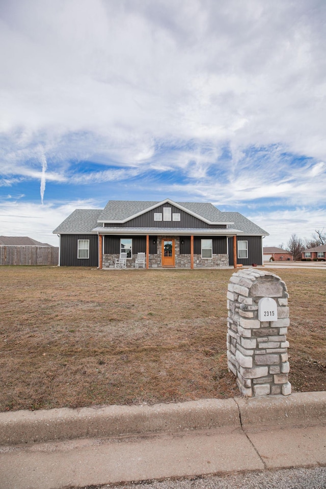 view of front of home with a shingled roof, covered porch, fence, and a front lawn