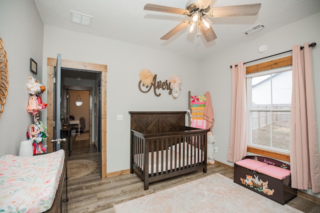 bedroom with visible vents, a crib, baseboards, and wood finished floors