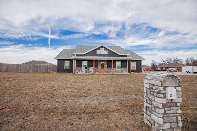 view of front of property featuring stone siding, a front lawn, roof with shingles, and fence