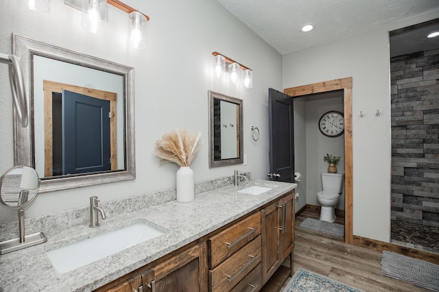 full bathroom with toilet, double vanity, a sink, and wood finished floors