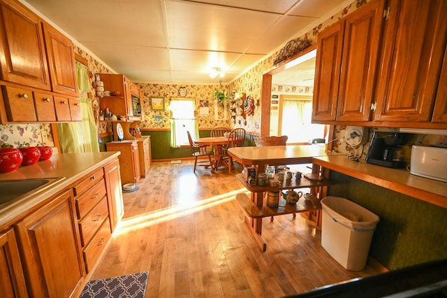 kitchen featuring a sink, wallpapered walls, brown cabinets, and light wood-style floors