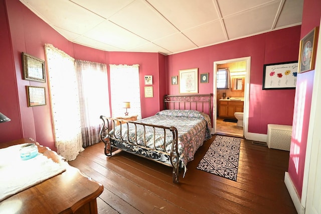 bedroom with wood-type flooring, a drop ceiling, and ensuite bath