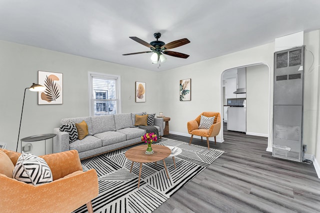 living area featuring baseboards, arched walkways, ceiling fan, and wood finished floors