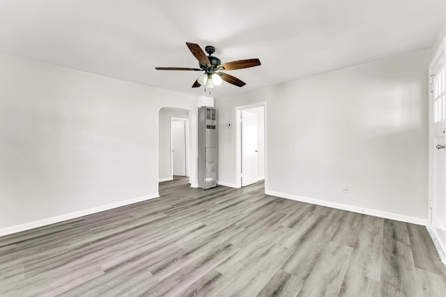 unfurnished bedroom featuring arched walkways, ceiling fan, wood finished floors, and baseboards