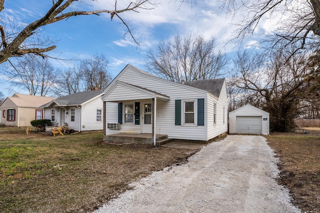 bungalow-style home featuring an outbuilding, covered porch, a detached garage, dirt driveway, and a front lawn