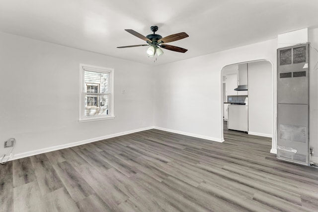 unfurnished room featuring arched walkways, ceiling fan, baseboards, and wood finished floors