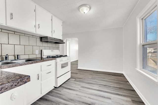 kitchen featuring arched walkways, under cabinet range hood, a sink, white range with gas cooktop, and light wood finished floors