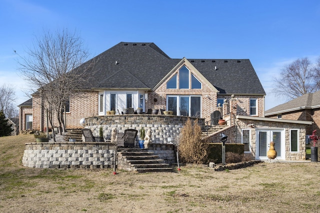 rear view of house featuring brick siding, roof with shingles, stairs, and a yard