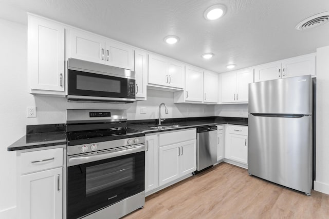 kitchen with light wood finished floors, stainless steel appliances, visible vents, white cabinets, and a sink