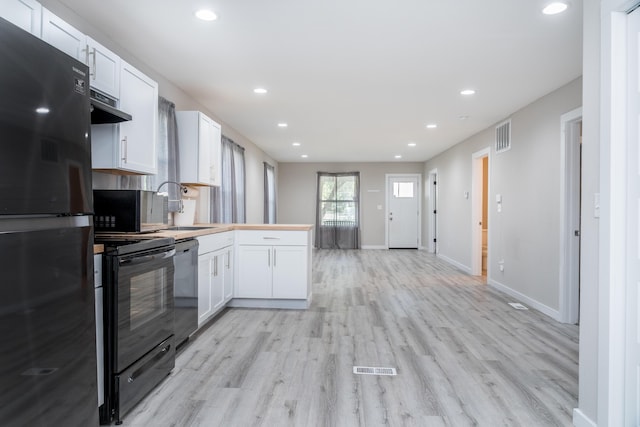 kitchen featuring under cabinet range hood, a sink, visible vents, white cabinets, and black appliances