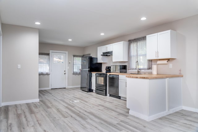 kitchen featuring light wood-style flooring, under cabinet range hood, butcher block counters, a sink, and black appliances