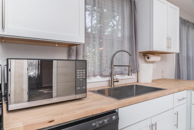 kitchen with wood counters, stainless steel microwave, white cabinets, and a sink