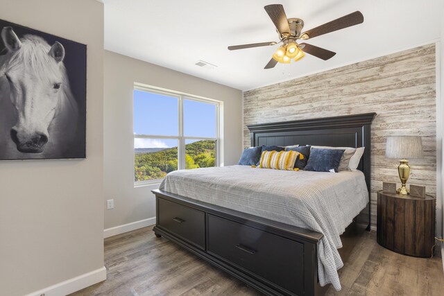 bedroom with an accent wall, visible vents, baseboards, and wood finished floors