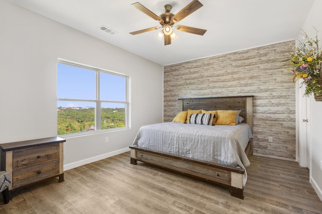 bedroom with baseboards, an accent wall, visible vents, and wood finished floors