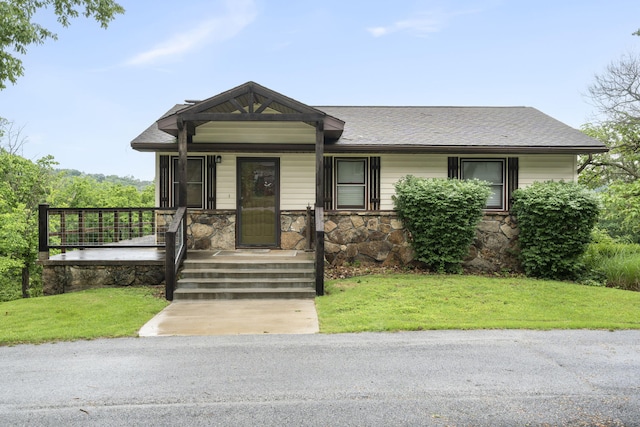 view of front facade featuring stone siding, roof with shingles, and a front lawn