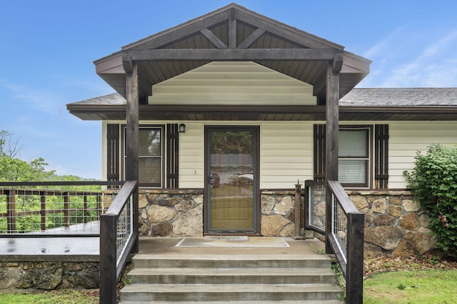 view of front of property featuring stone siding, covered porch, and roof with shingles