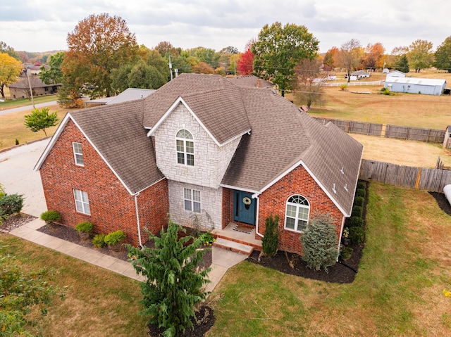 view of front of house featuring stone siding, roof with shingles, a front yard, and fence