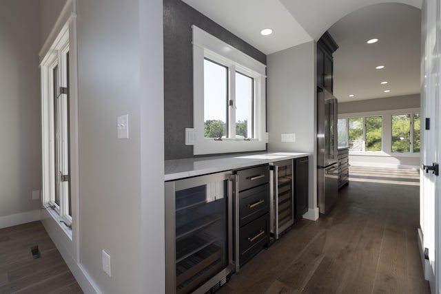 bar featuring dark wood-style floors, freestanding refrigerator, beverage cooler, and arched walkways