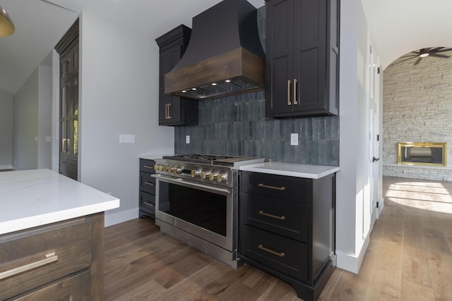 kitchen featuring dark wood finished floors, decorative backsplash, ceiling fan, custom range hood, and stainless steel stove