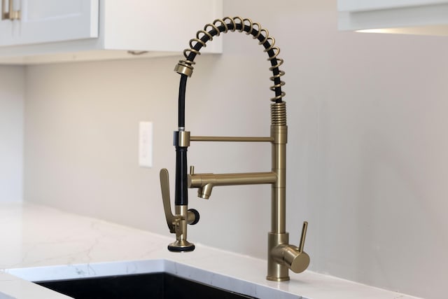 room details featuring light stone counters, a sink, and white cabinetry