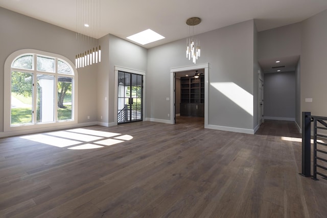 unfurnished living room featuring a skylight, a high ceiling, baseboards, and dark wood finished floors