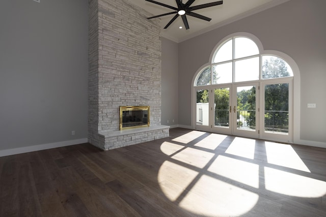 unfurnished living room featuring baseboards, ornamental molding, wood finished floors, and a stone fireplace