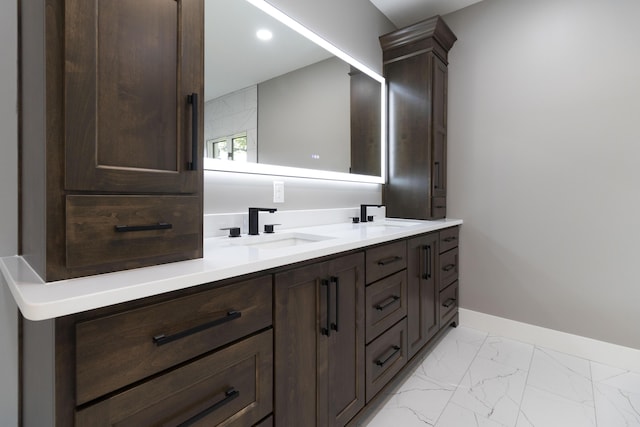 bathroom with marble finish floor, a sink, baseboards, and double vanity