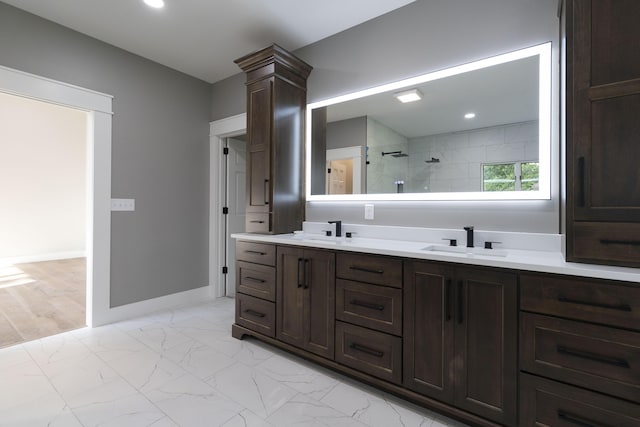 bathroom featuring marble finish floor, baseboards, a tile shower, and a sink