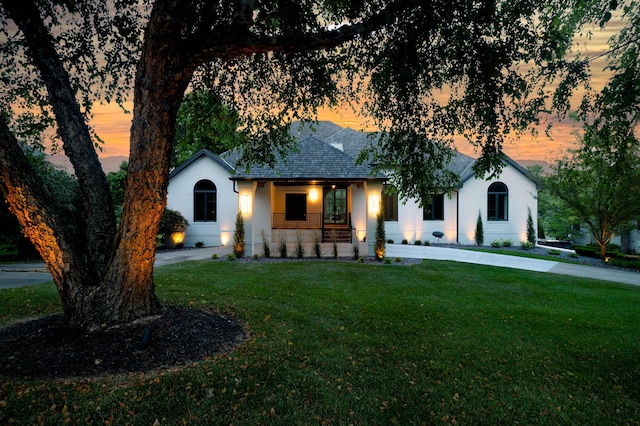 single story home with a shingled roof, covered porch, a yard, and stucco siding