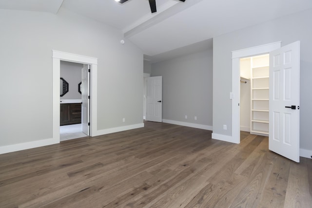 unfurnished bedroom with baseboards, wood finished floors, vaulted ceiling with beams, a spacious closet, and a closet