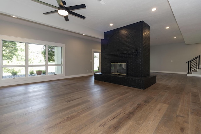 unfurnished living room with stairs, a brick fireplace, baseboards, and wood finished floors