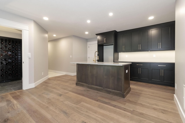 kitchen with light wood finished floors, a center island with sink, light countertops, and recessed lighting