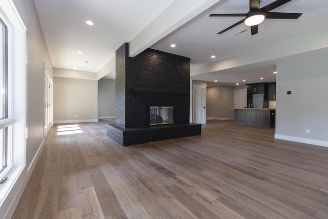 unfurnished living room featuring recessed lighting, a brick fireplace, wood finished floors, and baseboards