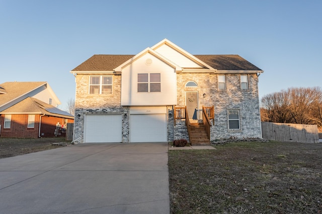 bi-level home with concrete driveway, an attached garage, fence, a front yard, and brick siding