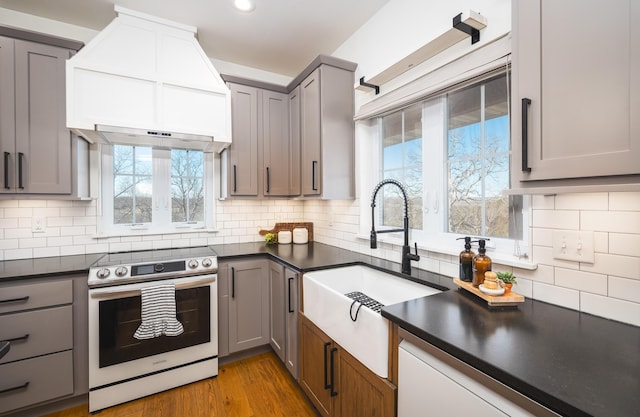 kitchen featuring dark countertops, gray cabinets, custom range hood, stainless steel range with electric cooktop, and a sink