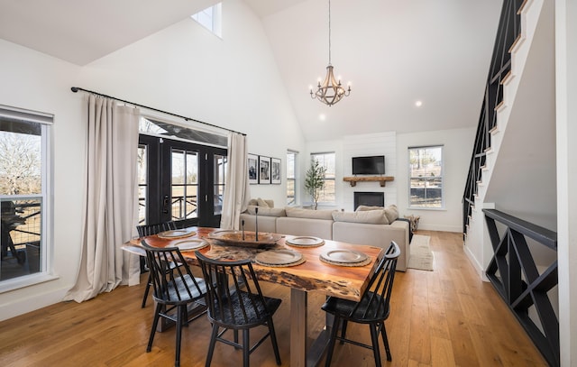 dining space featuring high vaulted ceiling, a large fireplace, light wood-style flooring, and an inviting chandelier