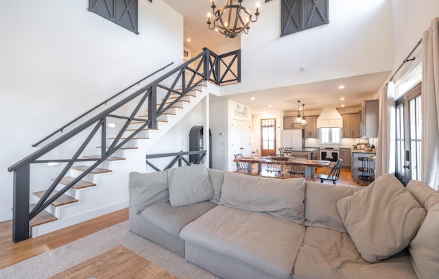 living area with light wood-style flooring, a towering ceiling, stairway, and baseboards