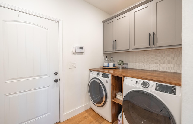 clothes washing area featuring baseboards, washer and clothes dryer, cabinet space, and light wood-style floors