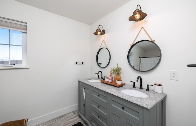 full bathroom featuring double vanity, baseboards, a sink, and wood finished floors