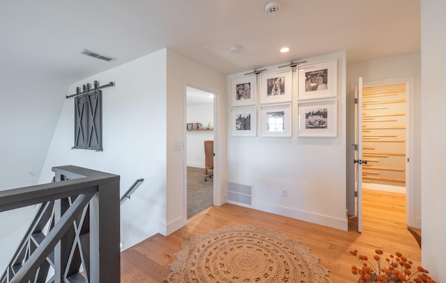 corridor featuring light wood finished floors, baseboards, visible vents, and an upstairs landing