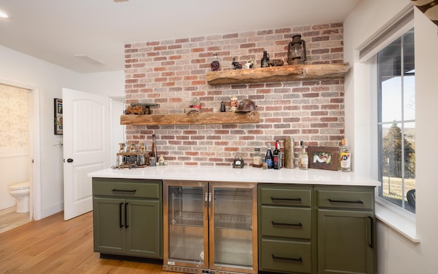 bar with a dry bar, light wood finished floors, beverage cooler, and brick wall