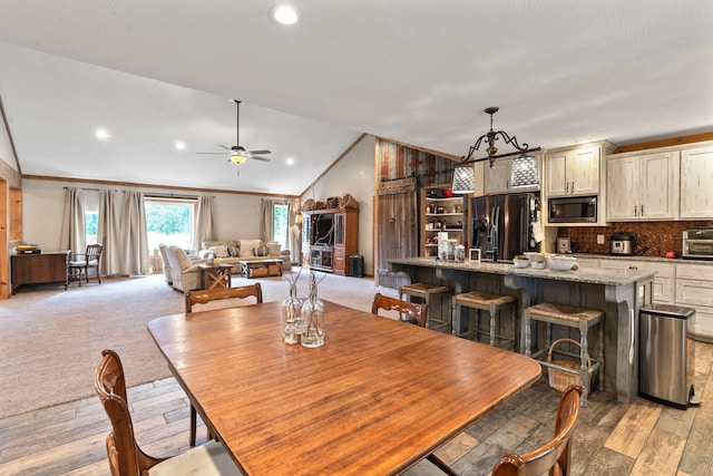 dining room featuring light wood finished floors, lofted ceiling, light colored carpet, ornamental molding, and ceiling fan