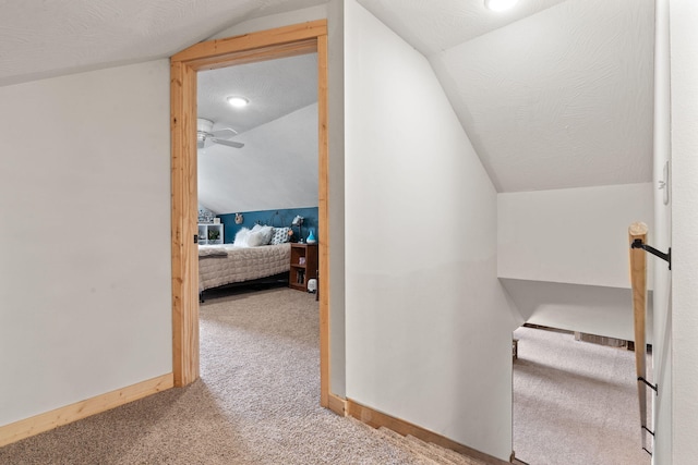 corridor with lofted ceiling, a textured ceiling, baseboards, and carpet flooring