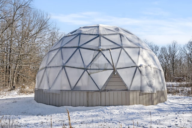 snow covered structure featuring a greenhouse and an outdoor structure