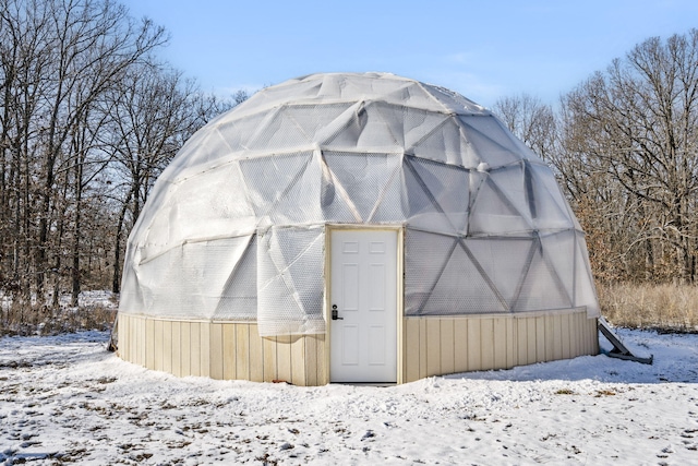 snow covered structure featuring an outbuilding and a greenhouse