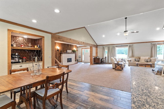 dining area featuring lofted ceiling, crown molding, a fireplace, and wood finished floors