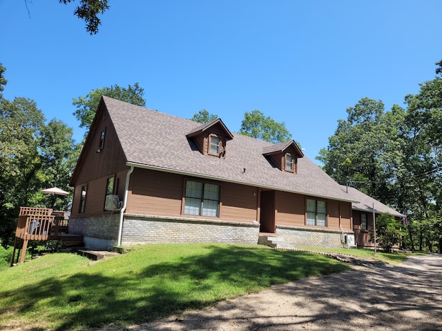 view of front of house with a shingled roof, a front yard, a deck, and brick siding