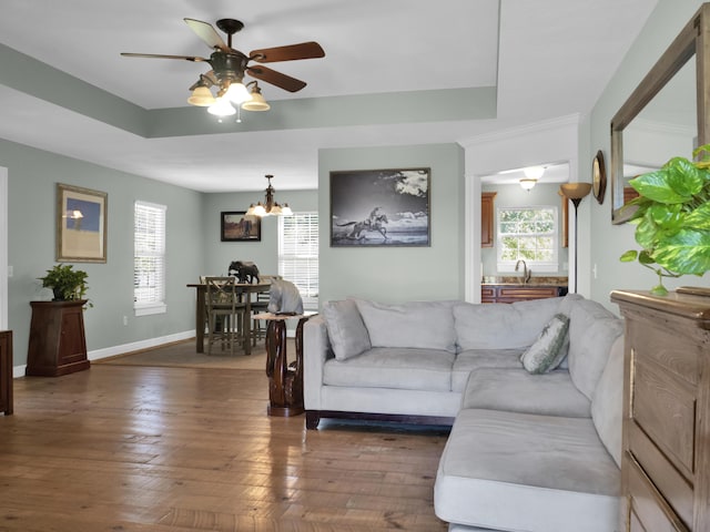 living room with dark wood-style floors, a tray ceiling, baseboards, and ceiling fan with notable chandelier